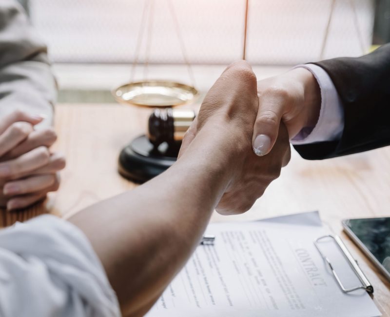 Close up of lawyer hand and man client shaking hand collaborate on working agreements with contract documents at the office.