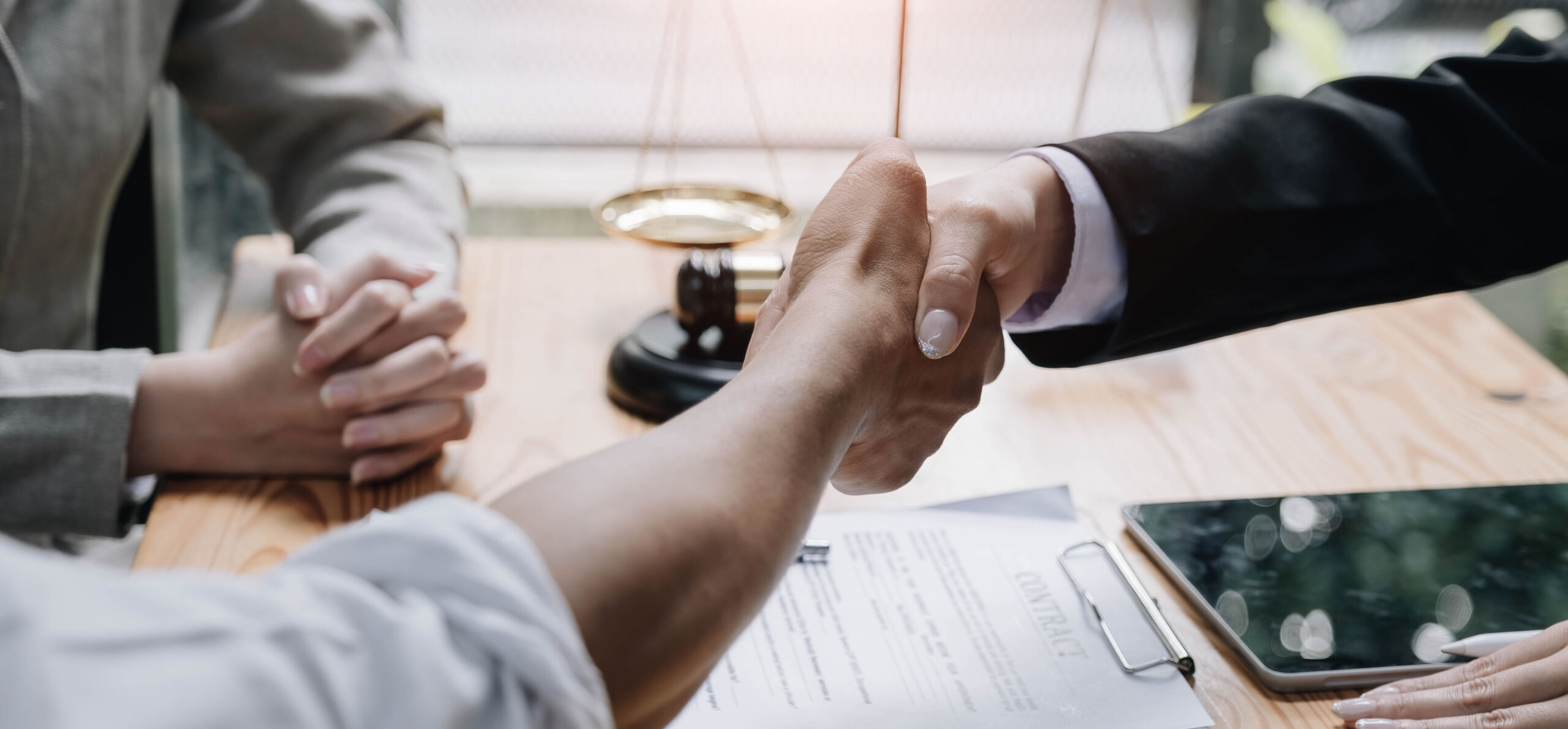 Close up of lawyer hand and man client shaking hand collaborate on working agreements with contract documents at the office.